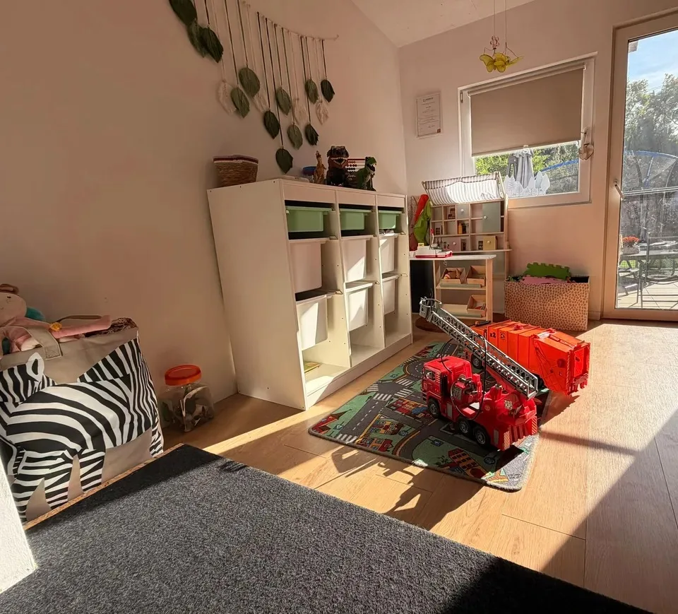 Sonniger Spielbereich mit Regalen, Spielzeug und Zugang nach draußen